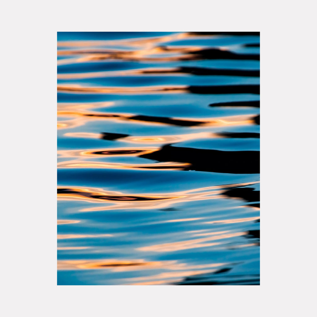 The artwork "Shimmer" by Kyle Murphy in gallery position 1 captures an abstract close-up of reflective water ripples bathed in vibrant blue and warm golden hues. The fluid, undulating shapes blend the impressionistic light play of Claude Monet with the serene abstraction reminiscent of Helen Frankenthaler’s color fields, evoking a tranquil yet dynamic atmosphere.