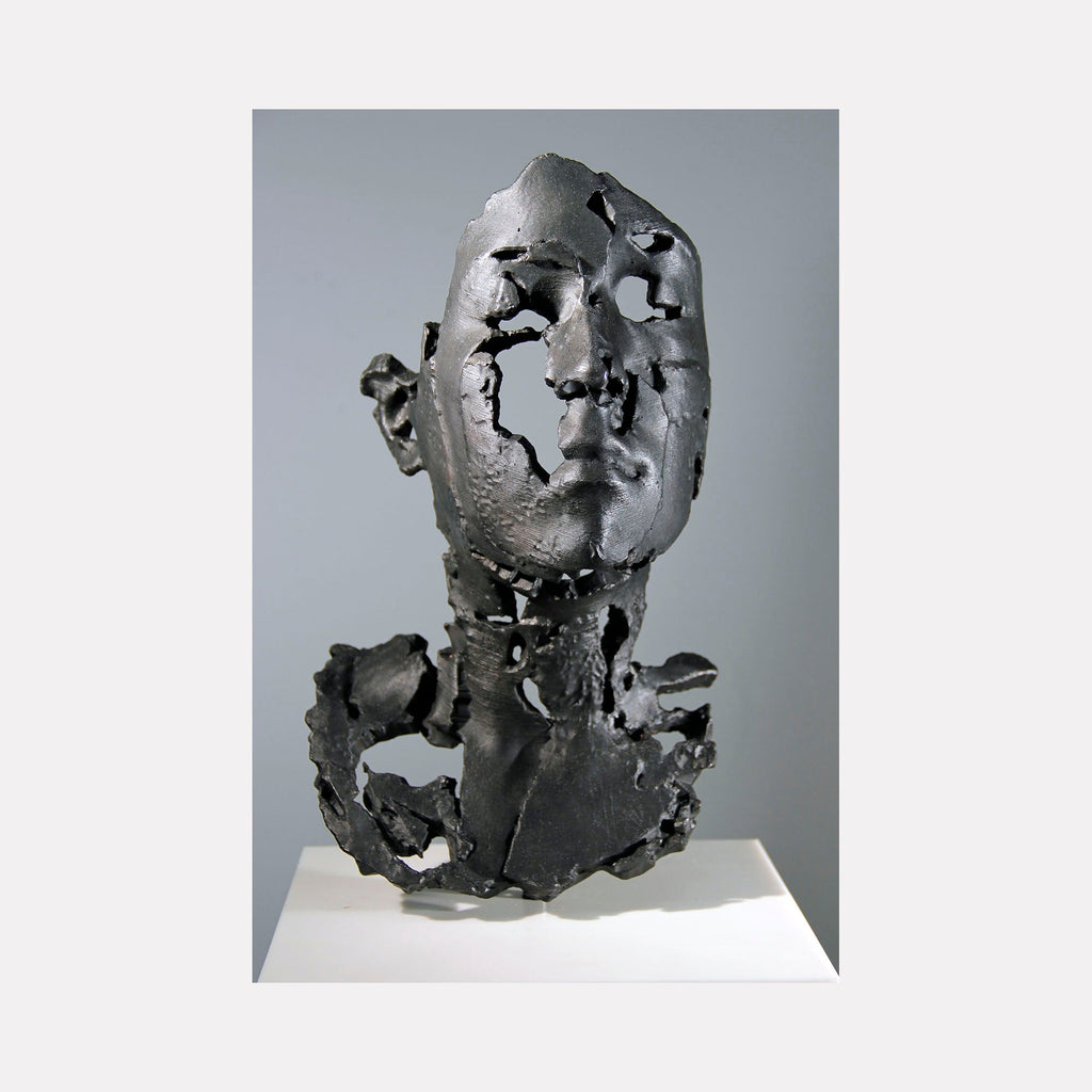 The artwork "L Degrade" by Sophie Kahn features a fragmented, textured gray metal sculpture of a human head and neck with deliberate erosion and negative spaces. The raw, industrial aesthetic and broken surfaces evoke themes of decay and transformation, reminiscent of the expressive distortions found in Alberto Giacometti’s sculptures and the deconstructed forms of Lucio Fontana.