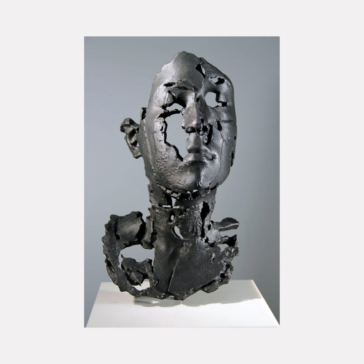The artwork "L Degrade" by Sophie Kahn features a fragmented, textured gray metal sculpture of a human head and neck with deliberate erosion and negative spaces. The raw, industrial aesthetic and broken surfaces evoke themes of decay and transformation, reminiscent of the expressive distortions found in Alberto Giacometti’s sculptures and the deconstructed forms of Lucio Fontana.
