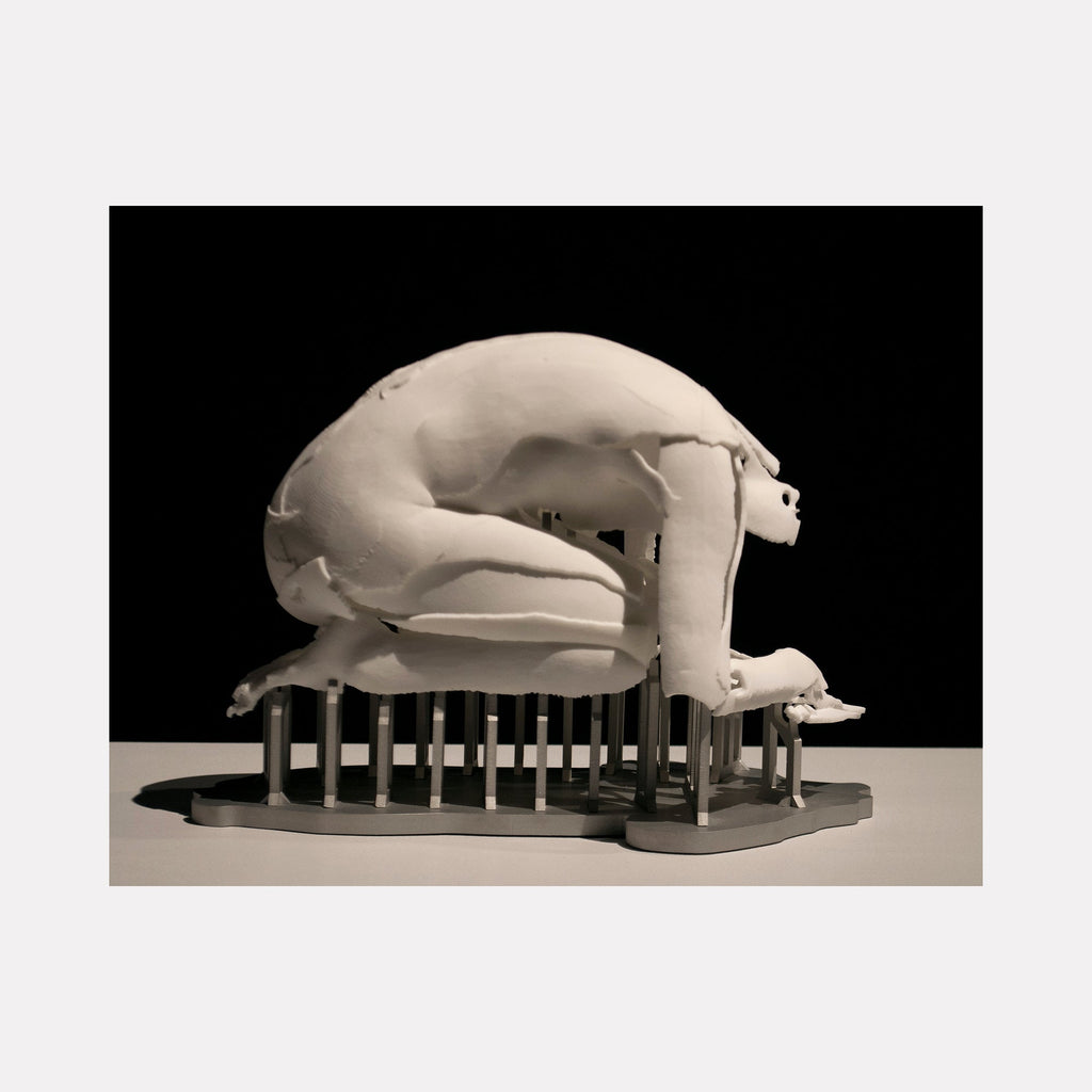 The artwork "Periode De Delire" by Sophie Kahn features a monochromatic sculpture of a fragmented, crouching human figure supported by vertical rods. The broken, textured surface and suspended posture evoke themes of vulnerability and fragility, reminiscent of the expressive distortion found in works by Alberto Giacometti and Louise Bourgeois.