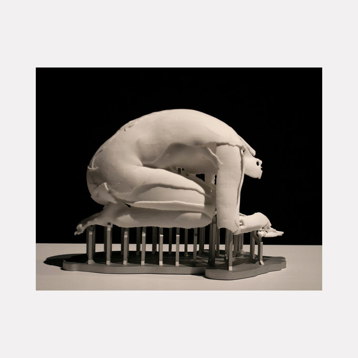 The artwork "Periode De Delire" by Sophie Kahn features a monochromatic sculpture of a fragmented, crouching human figure supported by vertical rods. The broken, textured surface and suspended posture evoke themes of vulnerability and fragility, reminiscent of the expressive distortion found in works by Alberto Giacometti and Louise Bourgeois.