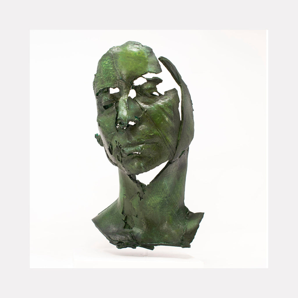 The artwork "Portrait of J Pthalo" by Sophie Kahn features a fragmented green sculpture of a human face and neck with eroded, textured surfaces and hollowed eyes. The abstract, weathered form evokes a sense of decay and memory, reminiscent of Alberto Giacometti’s expressive figurative sculptures and the raw materiality found in contemporary modernism.