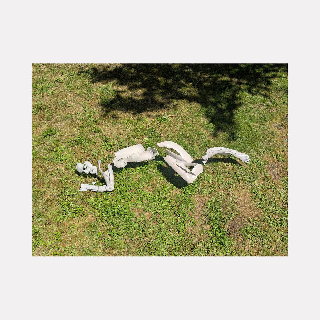 The artwork "Reclining Figure" by Sophie Kahn features a fragmented white sculpture of a reclining human form laid on grass, emphasizing abstract, skeletal shapes with smooth textures. The piece evokes the deconstructed, expressive qualities reminiscent of Henry Moore’s organic forms and the contemporary reinterpretations of human anatomy.