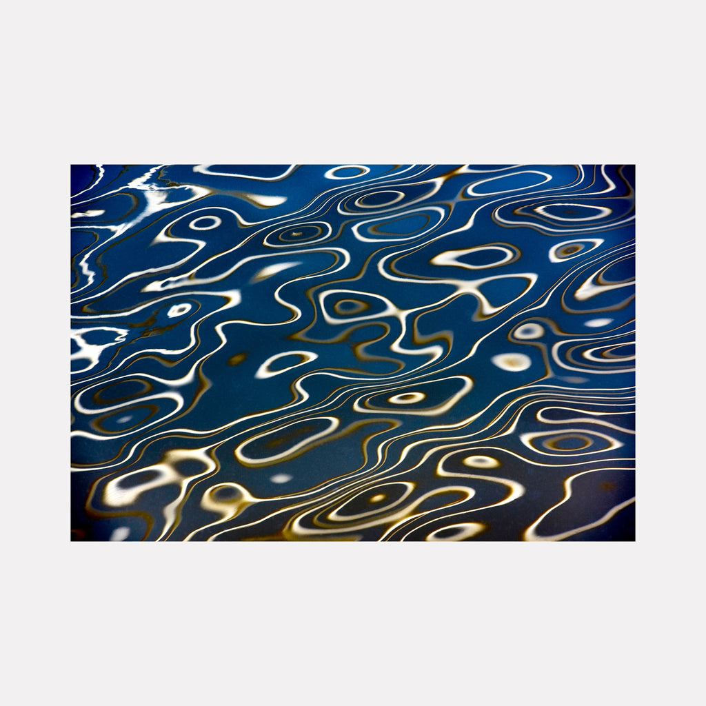 Surface Tensions 02 by Steve Edson reveals a mesmerizing abstract pattern of fluid, undulating lines in luminous white and gold tones swirling over a deep blue backdrop, evoking the delicate ripples and shimmering reflections on water with a contemporary, dynamic elegance.