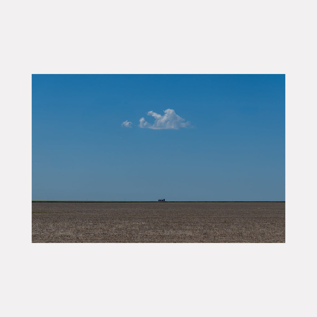 The artwork 'The Soul Cloud' by Dennis Maida captures a minimalist landscape photograph featuring a solitary white cloud floating in a vast azure blue sky above a stark brown plowed field. The horizon line creates a striking geometric composition, emphasizing the vast emptiness and serene simplicity of rural agricultural terrain by Dennis Maida.