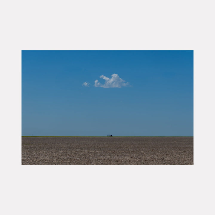 The artwork 'The Soul Cloud' by Dennis Maida captures a minimalist landscape photograph featuring a solitary white cloud floating in a vast azure blue sky above a stark brown plowed field. The horizon line creates a striking geometric composition, emphasizing the vast emptiness and serene simplicity of rural agricultural terrain by Dennis Maida.