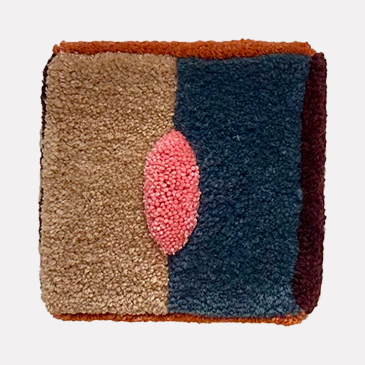 The artwork "Untitled" features a textured, rectangular design with a central oval shape in vibrant pink. It is divided into distinct color blocks of beige, deep blue, rust, and dark burgundy, showcasing a rich, tactile fabric composition with a cozy and plush appearance. By Ana Maria Farina.