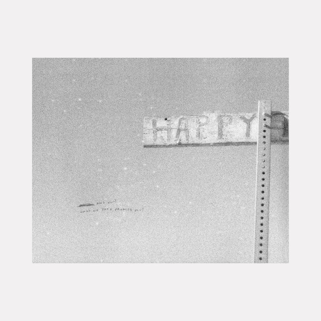 The artwork "What Did They Promise You" by Kelly McGovern features a grainy black and white photograph emphasizing a weathered street sign with partially visible letters resembling "HAPPY," mounted on a perforated metal pole. The minimalistic, raw texture and stark contrast evoke elements reminiscent of early street photography and conceptual art styles akin to works by Robert Frank or Walker Evans.