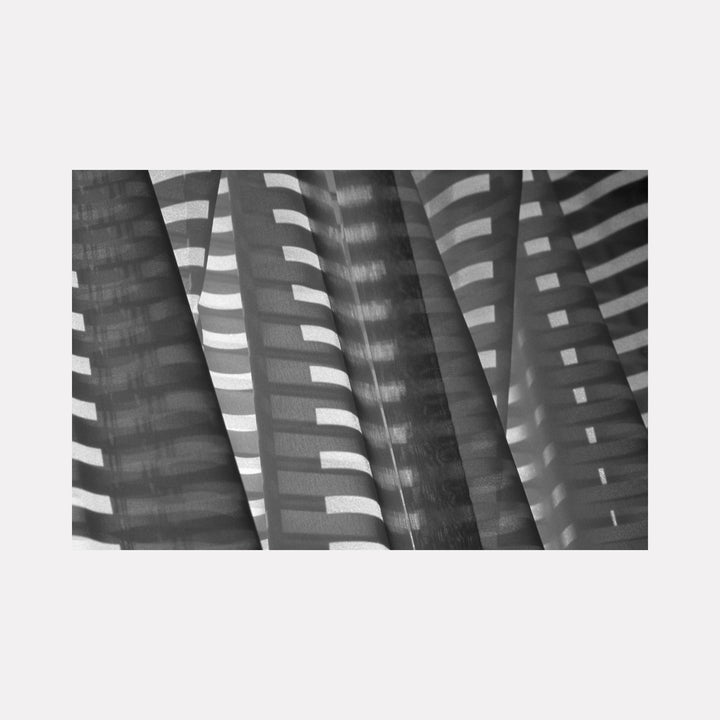 Window Light by Steve Edson features a delicate interplay of light and shadow cast through slatted blinds, creating rhythmic horizontal patterns on textured surfaces that highlight contrast and depth with a serene, contemplative atmosphere in monochromatic tones.