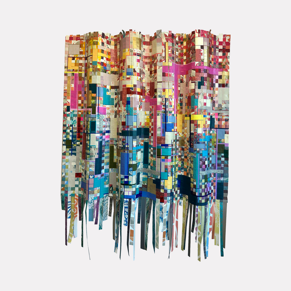 Woven Building Blocks by Shiri Phillips features an intricate assembly of multicolored fabric strips arranged in a cascading, grid-like pattern with rich textures and vibrant hues. The layered, tactile composition evokes a sense of depth and motion, blending handcrafted artistry with a contemporary abstract aesthetic.