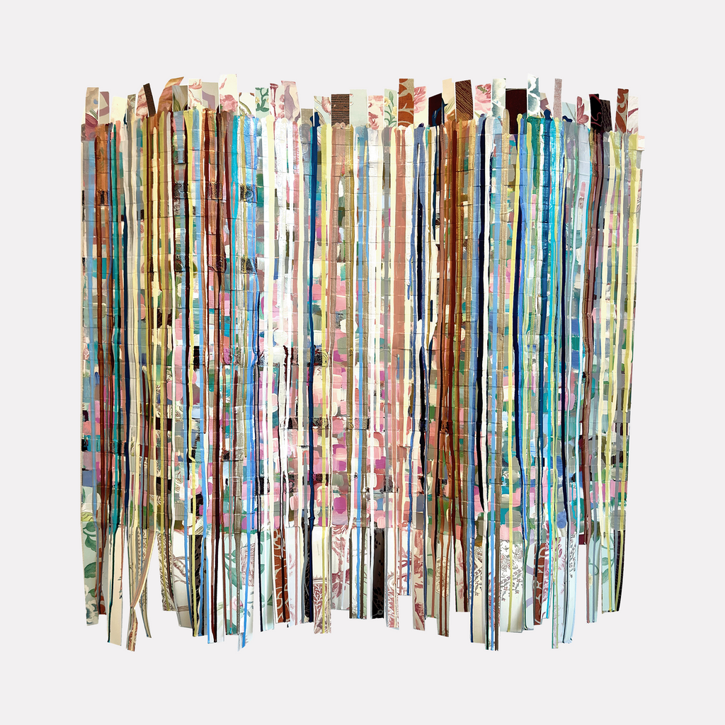Woven Lives by Shiri Phillips features delicate vertical strips of layered paper in soft pastels, earthy tones, and muted florals. The abstract assemblage creates a rhythmic, woven texture with a subtle interplay of color and pattern, evoking a sense of gentle movement and intricate craftsmanship in a contemporary design.