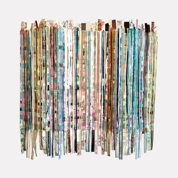 Woven Lives by Shiri Phillips features delicate vertical strips of layered paper in soft pastels, earthy tones, and muted florals. The abstract assemblage creates a rhythmic, woven texture with a subtle interplay of color and pattern, evoking a sense of gentle movement and intricate craftsmanship in a contemporary design.