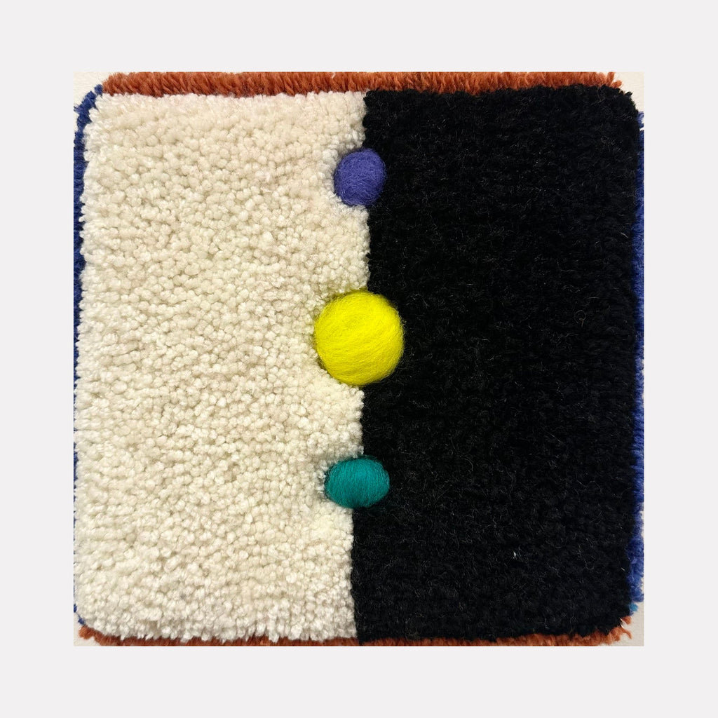 The artwork "Cosmic" features a textured, tufted design divided into two contrasting halves: a cream-colored side and a deep black side. Three vibrant, raised spheres in purple, yellow, and teal are aligned vertically along the center. The piece displays a tactile, plush texture with a modern abstract style by Ana Maria Farina.