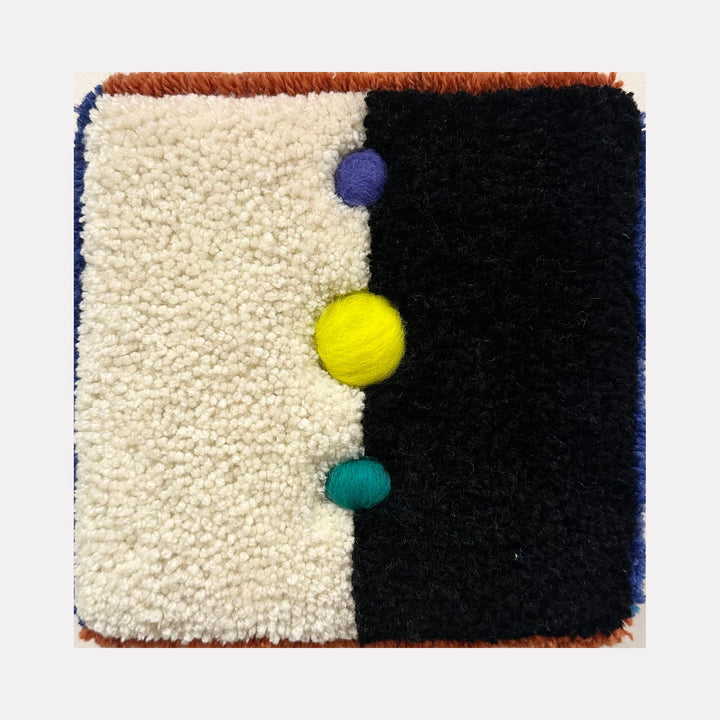 The artwork "Cosmic" features a textured, tufted design divided into two contrasting halves: a cream-colored side and a deep black side. Three vibrant, raised spheres in purple, yellow, and teal are aligned vertically along the center. The piece displays a tactile, plush texture with a modern abstract style by Ana Maria Farina.