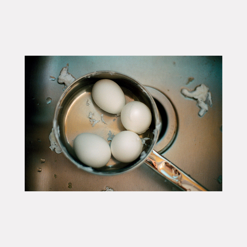 The artwork 'eggs' shows white eggs in a vintage silver pot with splashing water, captured in film photography by Esther Voisin