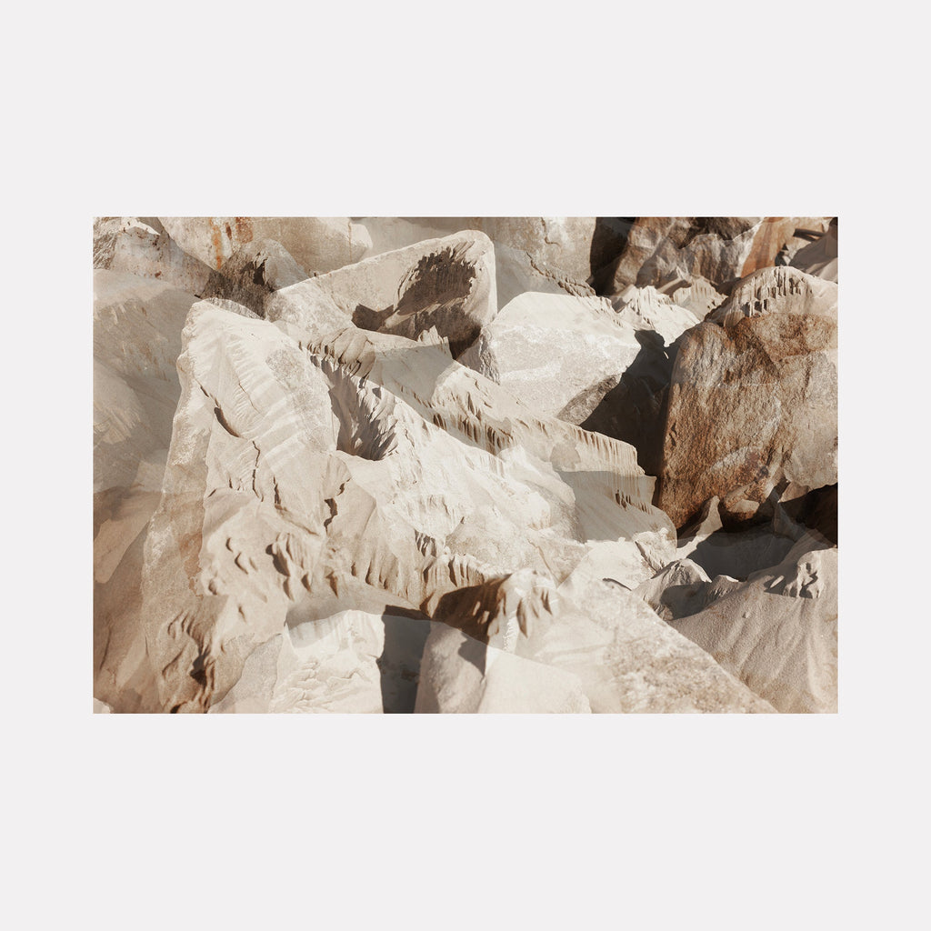 The artwork "erosion 2" by Eunice Pais portrays a layered landscape of pale, weathered rock formations with soft shadows and subtle earthy tones. The textured surfaces evoke natural erosion processes, reminiscent of the tactile land art of Richard Long and the serene minimalism found in the works of Agnes Martin.