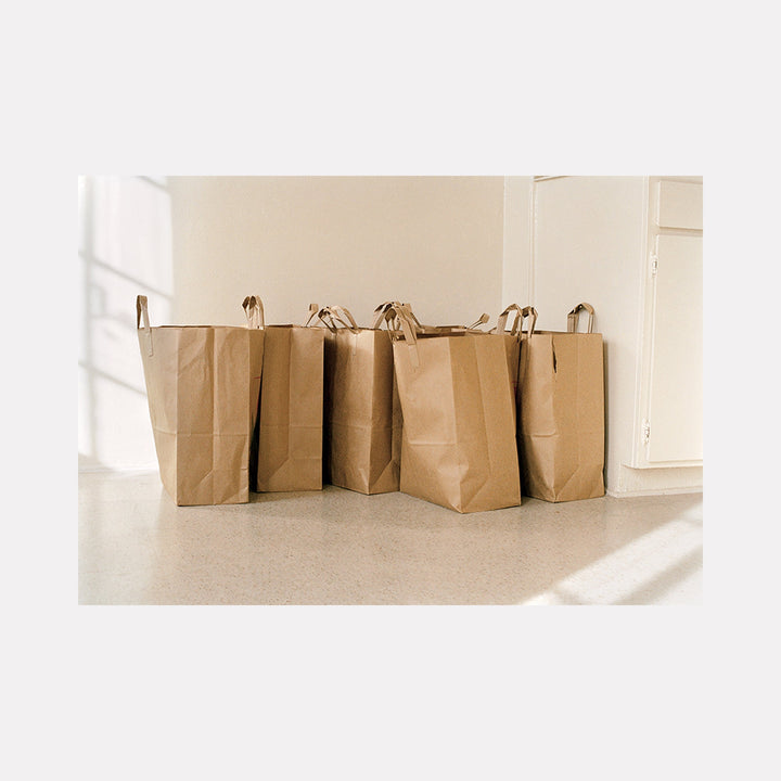 soulkitchen by Esther Voisin: Row of kraft paper shopping bags casting soft shadows on beige floor, minimalist film photography