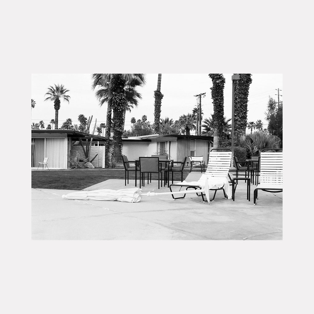 whitewind: Black and white film photo of mid-century motel patio with palm trees, lounge chairs and outdoor furniture by Esther Voisin