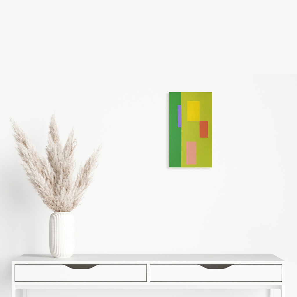The artwork 'Moments I (Triptych)' by Shyun Song features geometric color blocks in vibrant green, yellow, and soft pink arranged in a minimalist composition. A small oil painting on canvas displaying abstract rectangular shapes against a white background, complemented by dried pampas grass in a white vase below.