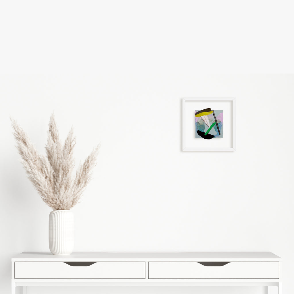 The artwork 'Fragment#05' by Winnie Sidharta features abstract geometric shapes in watercolor and magazine collage. A white frame contains bold angular forms in teal, yellow, and lavender hues, creating dynamic movement across the 5x5 inch panel. The mixed media piece combines fluid watercolor techniques with sharp-edged paper elements.
