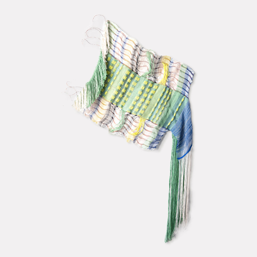 Loose English Morse Code by Kathie Halfin features a woven textile artwork blending cotton and flux yarn with copper wire. The piece displays an asymmetrical weave pattern in soft green, blue, and yellow hues, creating a wave-like texture. Delicate threads cascade from the top, while a longer fringe extends from one side, measuring 52 by 21.5 inches.