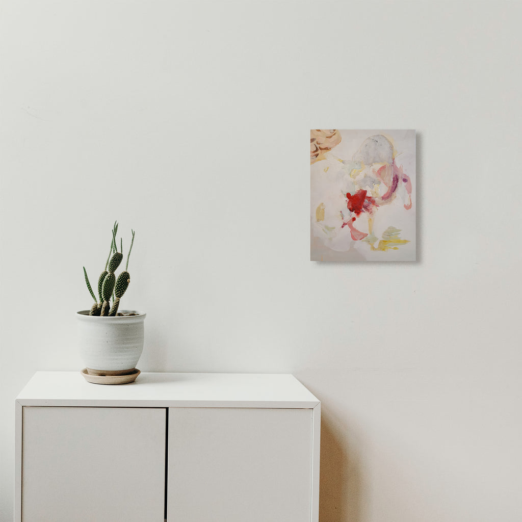 The artwork 'Tinkerbell: Silvermist' by Linda Lee Nicholas features delicate abstract brushstrokes in soft pink, red, and pale yellow hues on a white canvas. The fluid, ethereal composition suggests movement with gentle watercolor-like effects, displayed above a modern white cabinet with a small cactus plant.