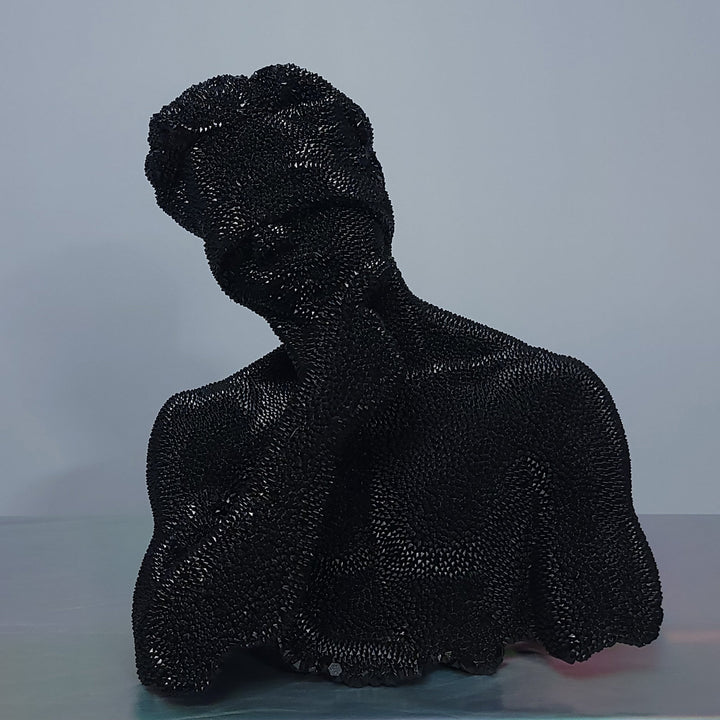 The artwork 'Thinking Blind - Original' by IvIvI features a glossy black resin sculpture depicting a contemplative silhouette. The textured surface creates a unique pattern of light reflections, giving depth to the minimalist form. The sculpture's distinctive pose and shiny black finish emphasizes introspection and artistic expression.
