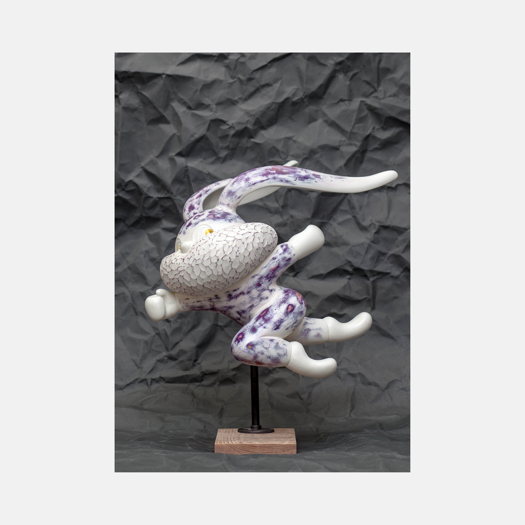 The artwork 'HOPE SPRINGS ETERNAL series' by Yusuke Ochiai features an abstract sculptural figure in white and purple tones, mounted on a wooden base. The resin sculpture displays a dynamic, flowing form with crackled texture and elegant curves, adorned with delicate purple splatters and 22k gold leaf details, set against a textured dark background.