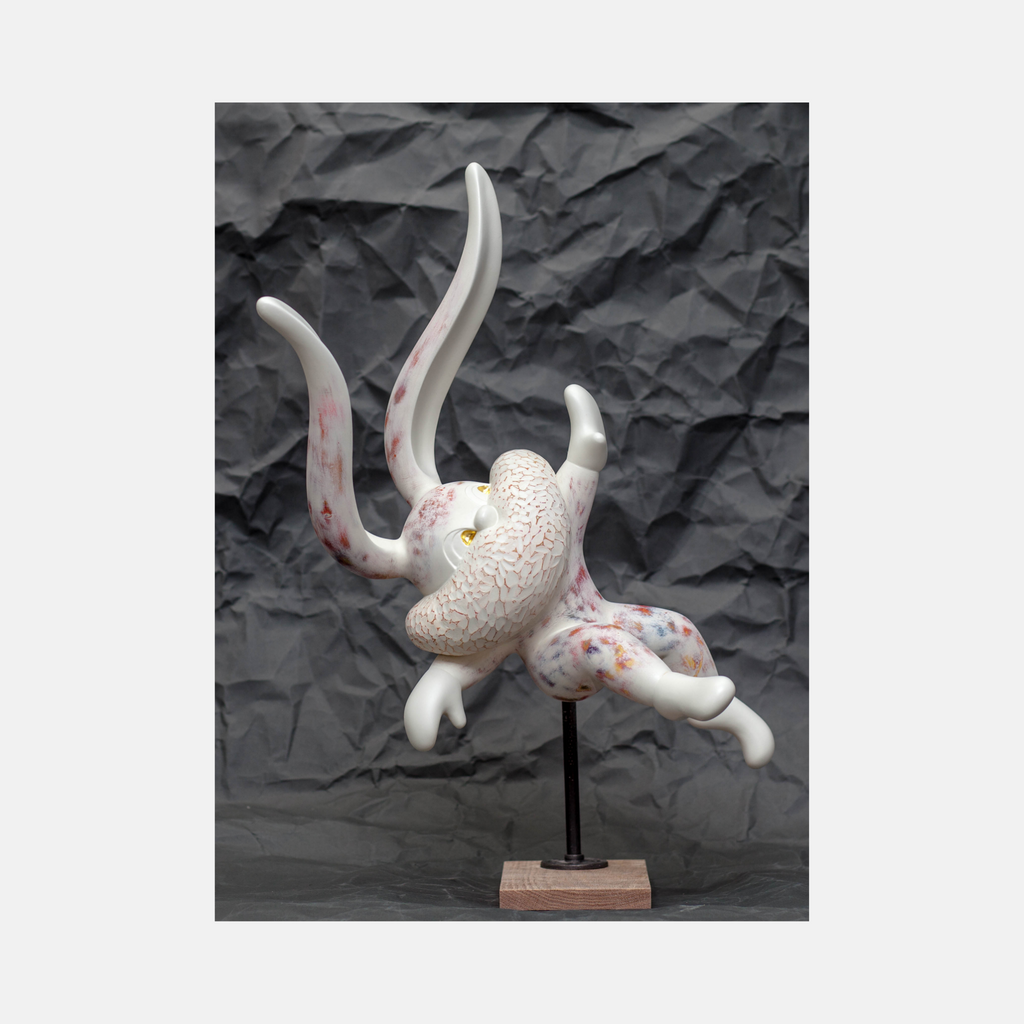 The artwork 'Hope Springs Eternal' by Yusuke Ochiai features an abstract sculptural form in white resin with delicate pink accents. The dynamic piece showcases curved, flowing tentacle-like extensions emerging from a textured central body, mounted on a metal stand with wooden base. The sculpture combines smooth and textured surfaces with 22k gold leaf details, set against a dark background.