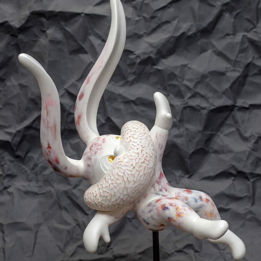 The artwork 'HOPE SPRINGS ETERNAL series' by Yusuke Ochiai features an abstract sculptural form in white resin with delicate pink accents and 22k gold leaf details. The piece showcases flowing, curved forms resembling organic movement, with a textured, crackled surface against a dark background. The sculpture exhibits dynamic curves and graceful undulations, mounted on a stand.