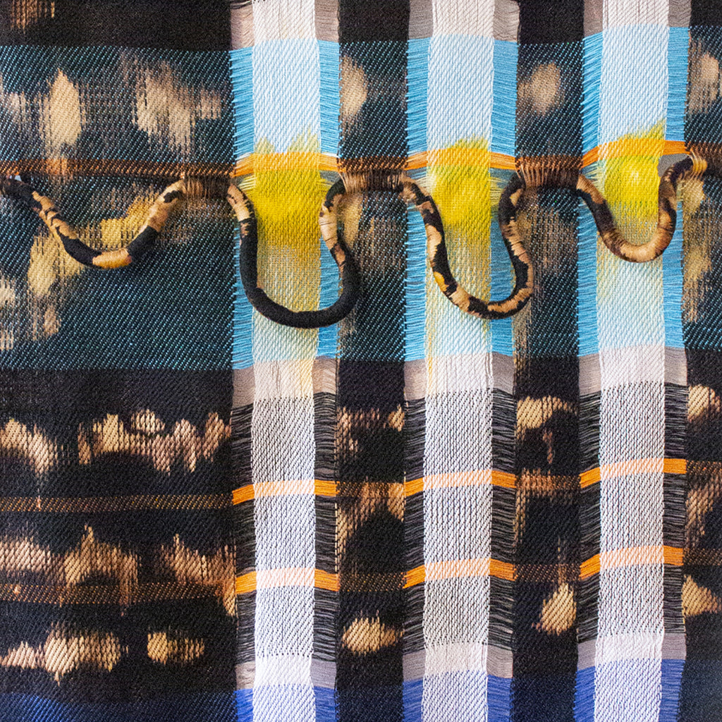 The artwork 'Fragments Of The Sky' by Kathie Halfin features a striking textile composition with vertical stripes in blue, yellow, and white, interwoven with copper rings. The piece combines plaid patterns and tie-dye effects in navy and tan, creating an abstract interpretation using cotton, nylon rope, and copper wire. The mixed-media textile artwork measures 65 by 35 inches. By Kathie Halfin.