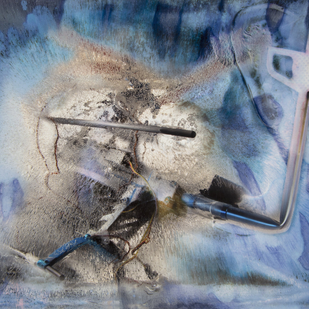 The artwork 'Crash in Blue' features abstract mixed media composition with dramatic contrasts of deep blues and silvery whites. Central metallic forms create dynamic tension against a stormy background, with textural elements suggesting industrial materials. Paint roller and tools visible in composition add raw, experimental quality. Mixed media on panel by Sarah Canfield.