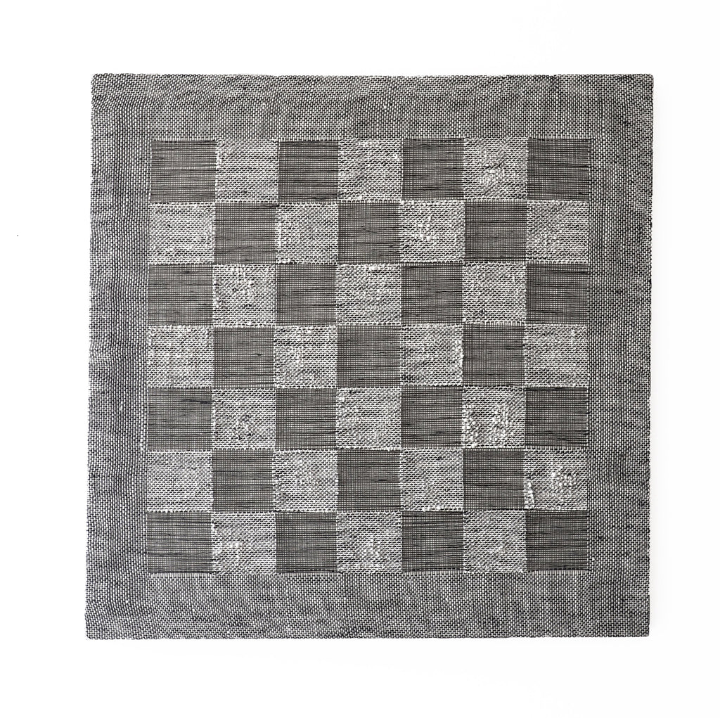 The artwork 'Checkerboard I' by Morgan Hale features a monochromatic square composition with alternating textured squares creating a classic checkerboard pattern. Handwoven linen and plaster combine to form deep and light gray squares, surrounded by a textured border. The 18x18 inch piece showcases intricate textile craftsmanship and dimensional surface texture.