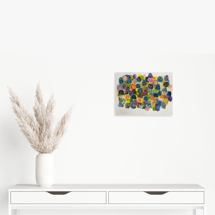 The artwork 'Community is Important' by Ayane Kurai features a vibrant cluster of abstract circular shapes in watercolor and cray-pas, rendered in blues, yellows, greens, and purples. The organic forms overlap and blend together on white paper, creating a dynamic composition suggesting unity and connection. Displayed above a modern white console with pampas grass decor.