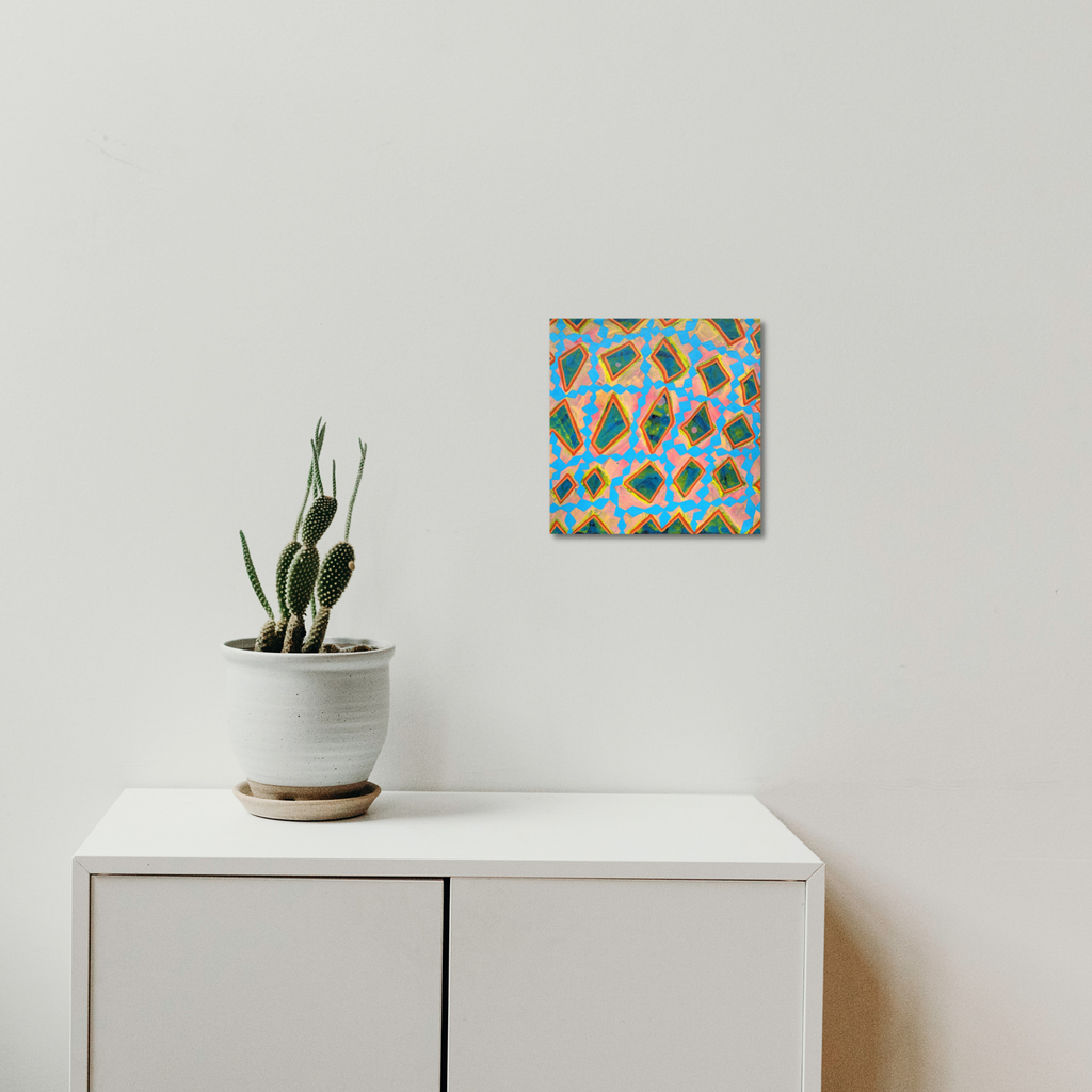 The artwork 'Composition No. 242' by Raul Ortiz features vibrant geometric patterns in turquoise blue and warm orange, creating a dynamic mosaic-like design on linen canvas. Abstract diamond shapes intersect and overlap in a repetitive pattern, displaying a modern minimalist aesthetic. The 12x12 inch acrylic painting hangs above a white cabinet beside a potted cactus.