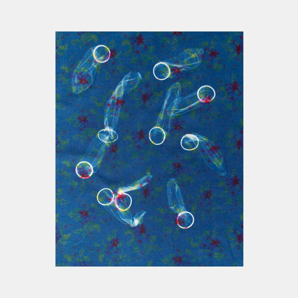 The artwork 'Condom Arrangement' by Warner Ball features ethereal cyanotype prints on fabric, displaying floating circular forms with wispy, translucent trails against a deep blue background. Small red star-like shapes scatter across the composition, creating a celestial effect. The ghostly white shapes appear to dance across the 20x16 inch textile surface.