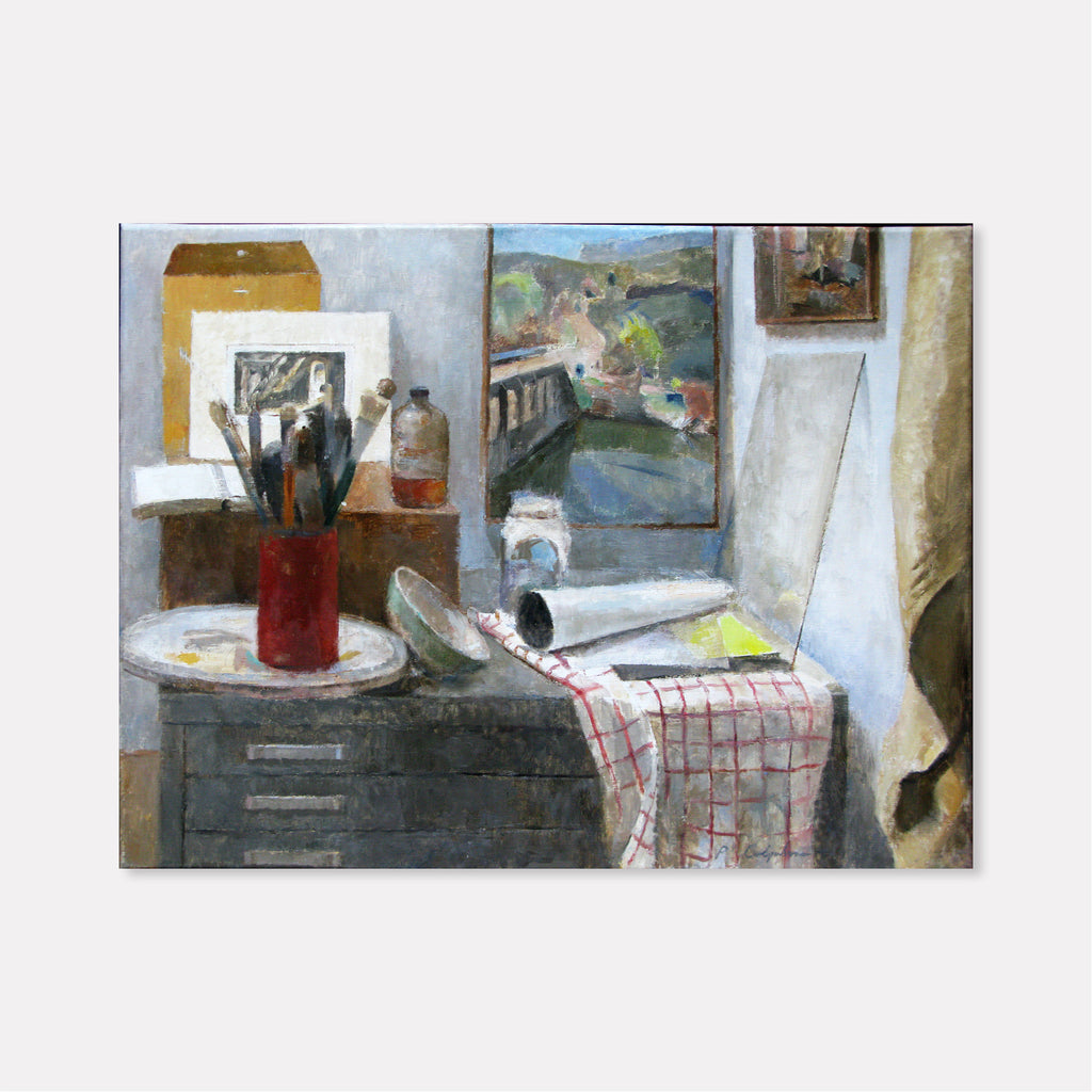 The artwork 'Corner of the Studio' by Peter Colquhoun depicts an artist's workspace with a dark wooden cabinet topped by a circular surface displaying art materials, brushes in a red holder, and framed artwork. A landscape painting hangs on the gray wall, while a checkered cloth drapes over the surface. Oil on linen, capturing intimate studio details with muted tones and masterful brushwork. By Peter Colquhoun.