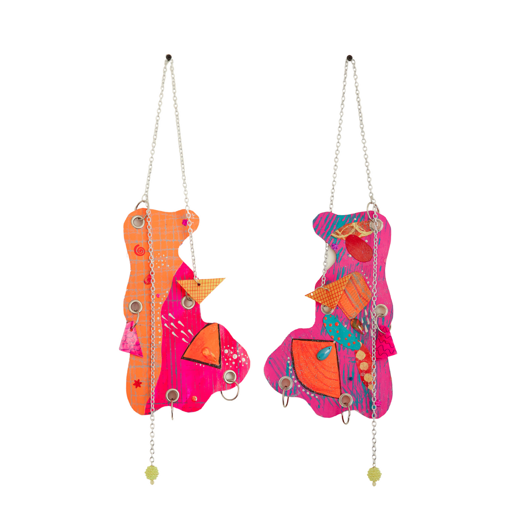 Duck Face by Sunny Chapman features vibrant abstract wall hangings in pink and orange, adorned with geometric shapes, metallic chains, and decorative elements. Mixed media artwork combining acrylic paint, glitter, jewels, and handmade charms creates a playful composition with layered textures and suspended beaded accents. By Sunny Chapman.