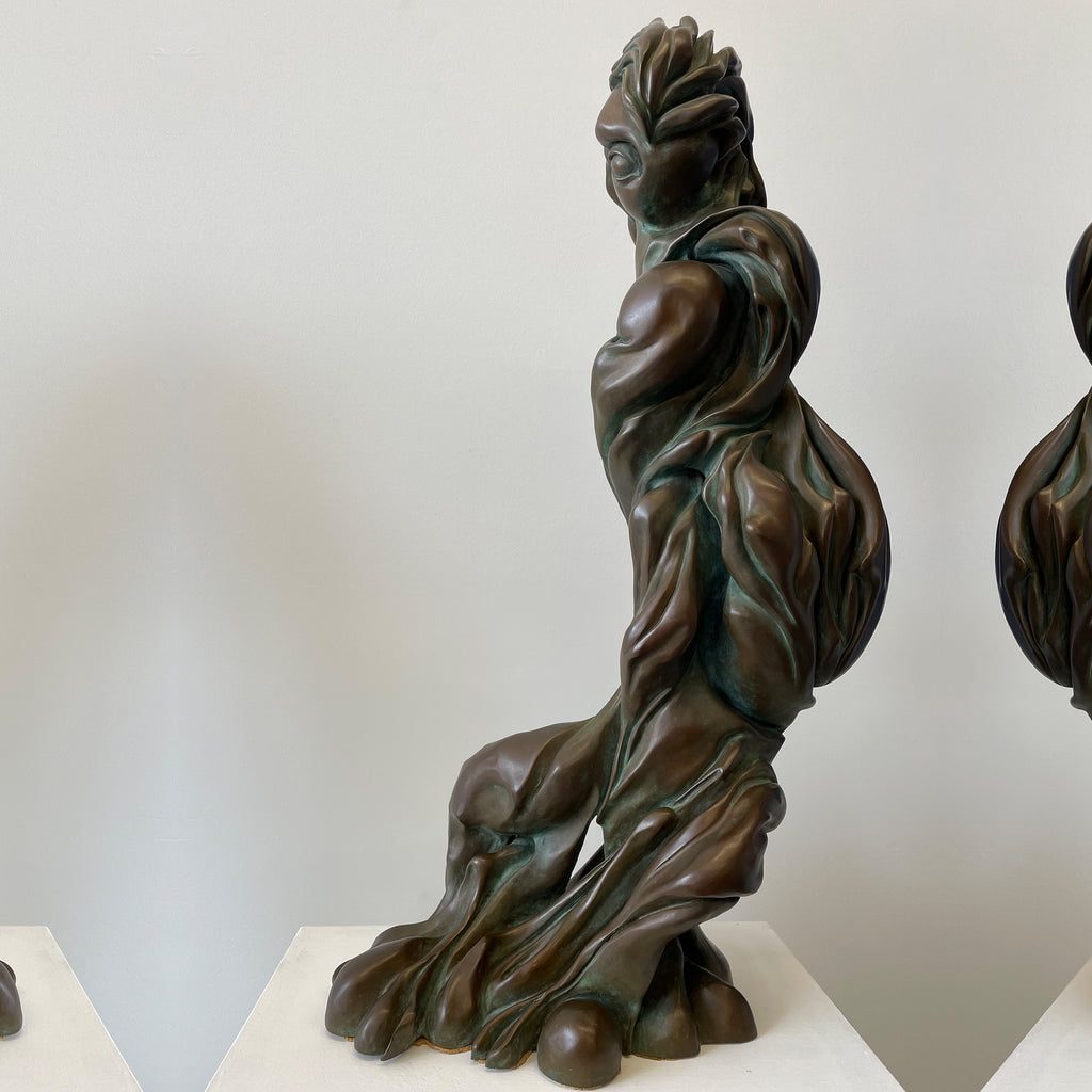 The artwork 'EYE' by Nora Chavooshian features a dynamic bronze sculpture with fluid, twisting forms. The abstract figure stands 27 inches tall, showcasing sweeping curves and organic movement. Deep patina in rich brown tones with verdigris highlights emphasizes the dramatic sculptural elements and flowing lines that spiral upward through the composition.