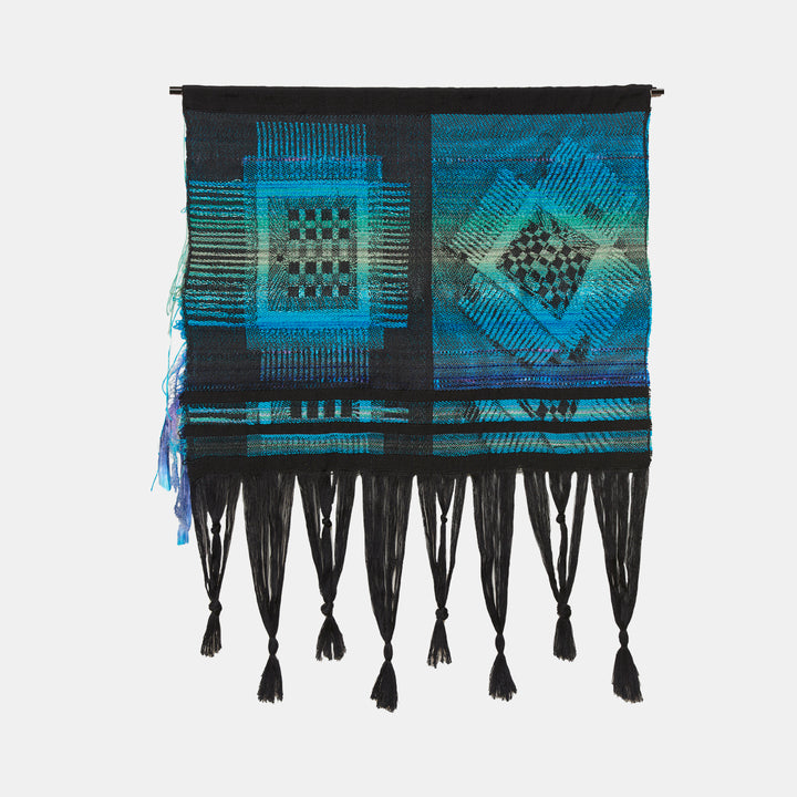 The artwork 'Eyes to See the Soul' by Robin Kang features geometric patterns woven in vibrant turquoise and deep blue hues. Abstract checkerboard motifs and linear elements create a digital-inspired design on hand jacquard woven cotton. Black tassels adorn the bottom edge, while metallic yarns add subtle shimmer throughout the contemporary textile artwork.