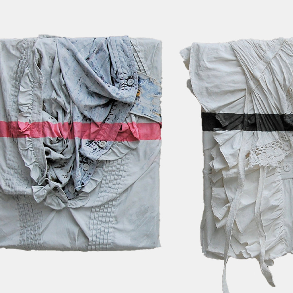 The artwork 'Family' by Noriko Okada features two abstract textile compositions side by side. Each piece showcases crumpled and pleated fabric in pale gray tones, with one adorned by a striking pink horizontal stripe and the other with a black band. The textured surfaces create dramatic shadows and folds, emphasizing the sculptural qualities of the oil-painted fabric.