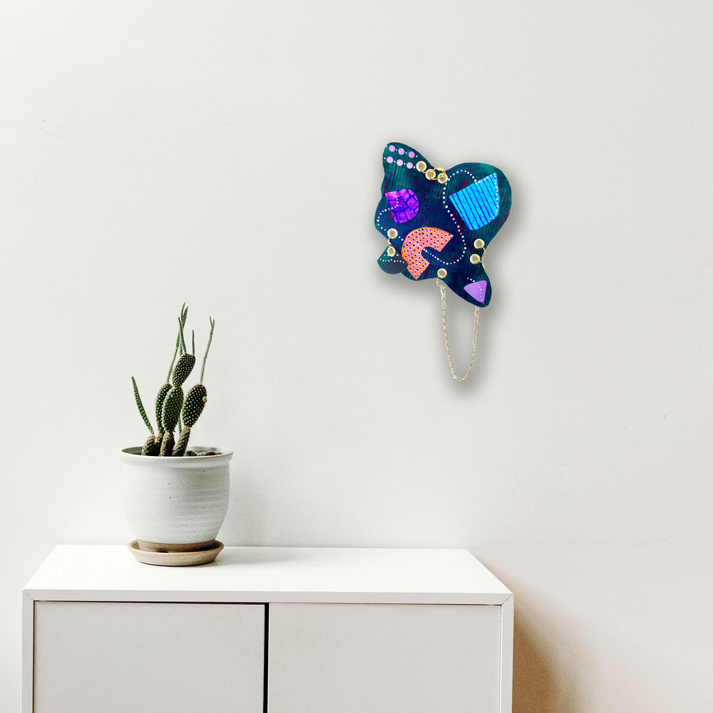 The artwork 'Feed' by Sunny Chapman features an abstract butterfly-shaped form in vibrant turquoise, pink, and purple hues with dotted accents. The acrylic painting on paper showcases geometric patterns and organic shapes, creating a modern, playful composition against a clean white background. 12x12 inches artwork by Sunny Chapman.