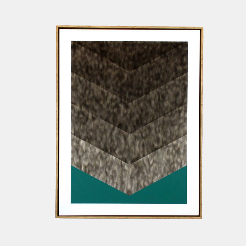 The artwork 'Foot Habits' by Evan Ishmael features a striking chevron pattern created with soot gradients, ascending from light to dark against a bold teal background. The textured, smoky effect creates depth through five distinct angular sections, framed in warm wood, showcasing the unique combination of soot and spray acrylic techniques.
