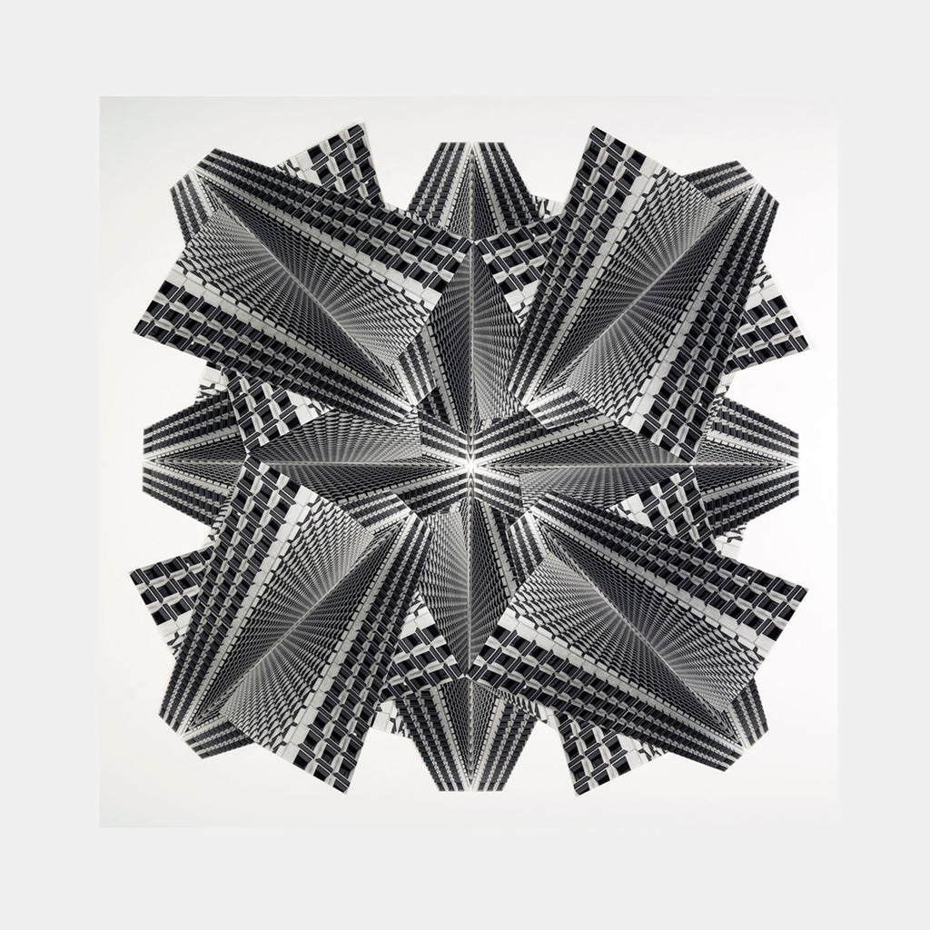 The artwork 'Galaxies' by Adrienne Moumin features a striking black and white kaleidoscopic collage pattern created from architectural photographs. Geometric lines radiate from a central point, forming an intricate star-like design with layered angular segments. The hand-cut gelatin silver prints create a mesmerizing optical illusion of depth and dimension.