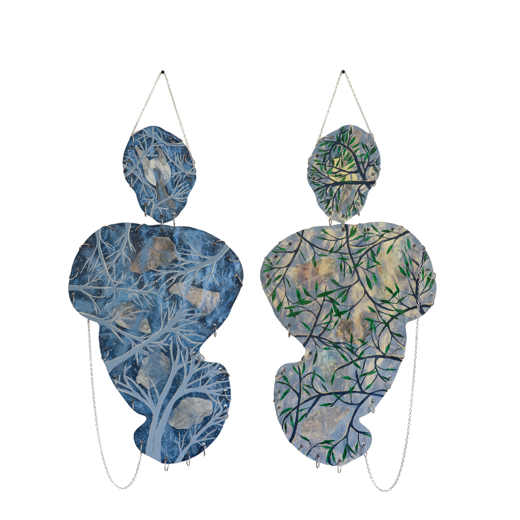 The artwork 'Grey Days/Dark Nights/Watching the Sky Through the Trees' by Sunny Chapman features two abstract organic shapes, one in muted blue with delicate fern-like patterns, the other in soft green with branching tree motifs. Both forms hang by metal chains, created with acrylic and collaged painted tissue on plywood, reflecting a dreamy, nature-inspired aesthetic.