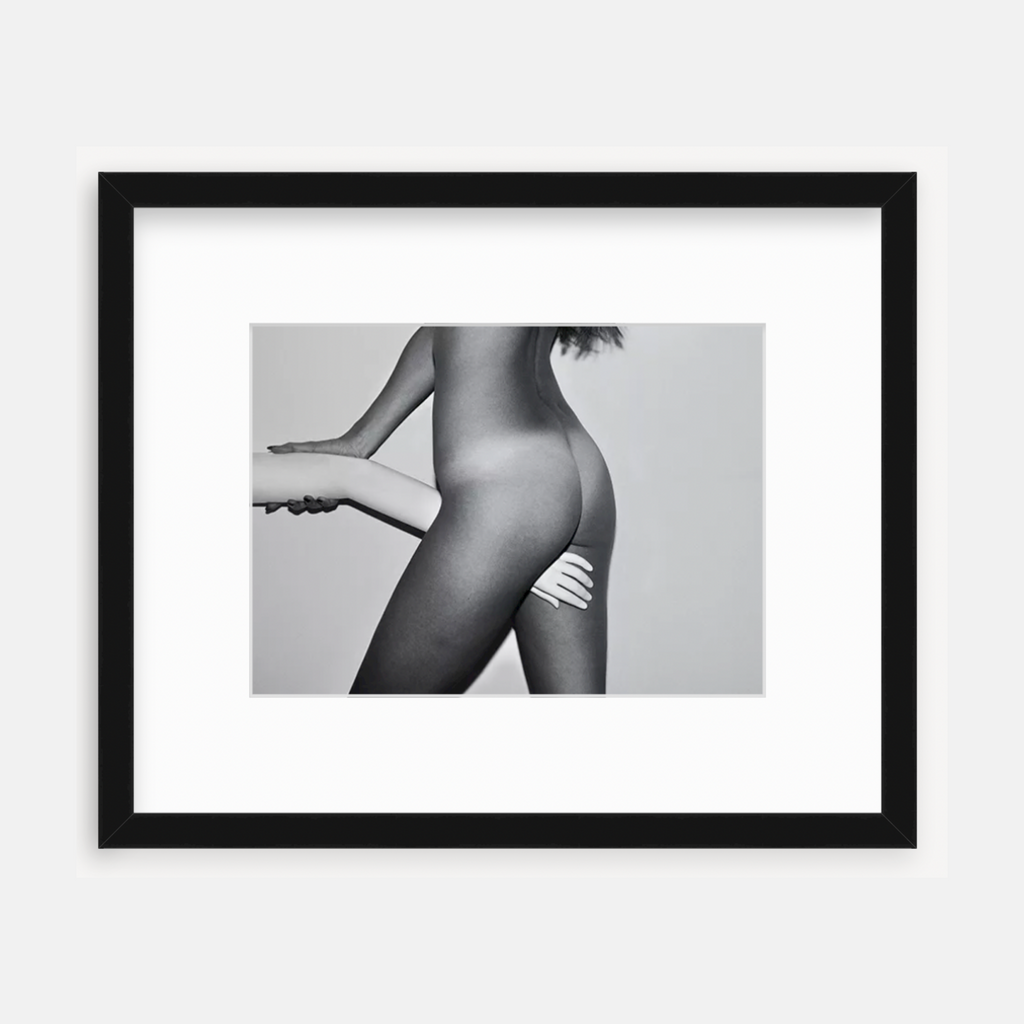 The artwork 'Hand in Between Legs' by Mari Sarai presents an artistic black and white photograph showcasing an abstract form with dramatic light and shadow. The composition features smooth contours and elegant lines, professionally matted and presented in a sleek black frame. The monochromatic technique enhances the sculptural quality and artistic expression.