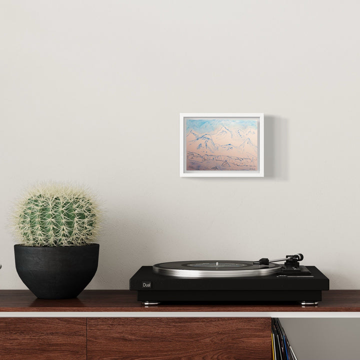 The artwork 'Damoy Point' by Ali Ha features delicate line drawings of flying birds against a soft pastel sky with shades of pink and blue. Created on Stonehenge warm white paper with precise Micron ink and Caran d'Ache strokes, displayed in a crisp white frame on gray wall above vintage turntable, beside potted cactus.
