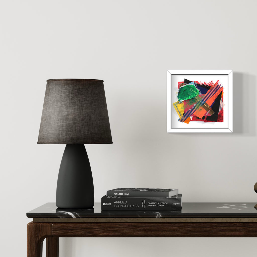 The artwork 'Origami Garden no.1' by Songyi Kim features vibrant abstract geometric shapes in green, red, and yellow, created through origami paper collage technique. The composition displays dynamic angles and layered textures, with bold strokes of washi tape adding depth and movement. Framed in white, the mixed media piece creates a striking modern botanical interpretation.