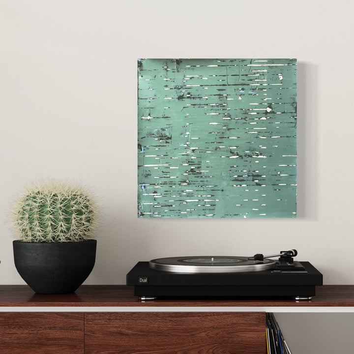 The artwork 'Drifting' by Shira Toren features a textured abstract composition in serene mint green with horizontal striations and subtle gray accents, created using Venetian plaster on panel. The surface evokes a weathered, organic feel with its layered, scratched appearance, measuring 16 x 16 inches.