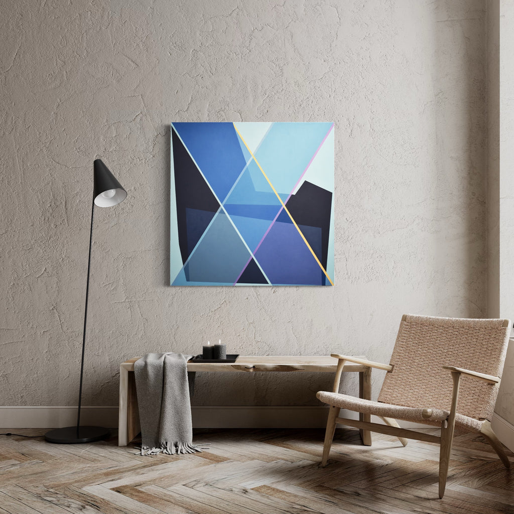 The artwork 'Staged X1' by Kati Vilim features a geometric abstract composition with intersecting triangular shapes in varying shades of blue, from deep navy to light azure, accented by subtle yellow lines. The oil painting on canvas creates a modern, minimalist aesthetic with sharp angular forms and clean lines.